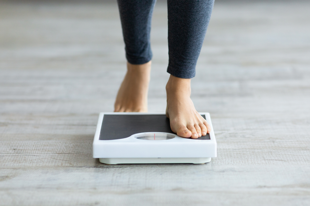 Woman standing on a digital scale to see the effectiveness of kratom weight gain reversal efforts.